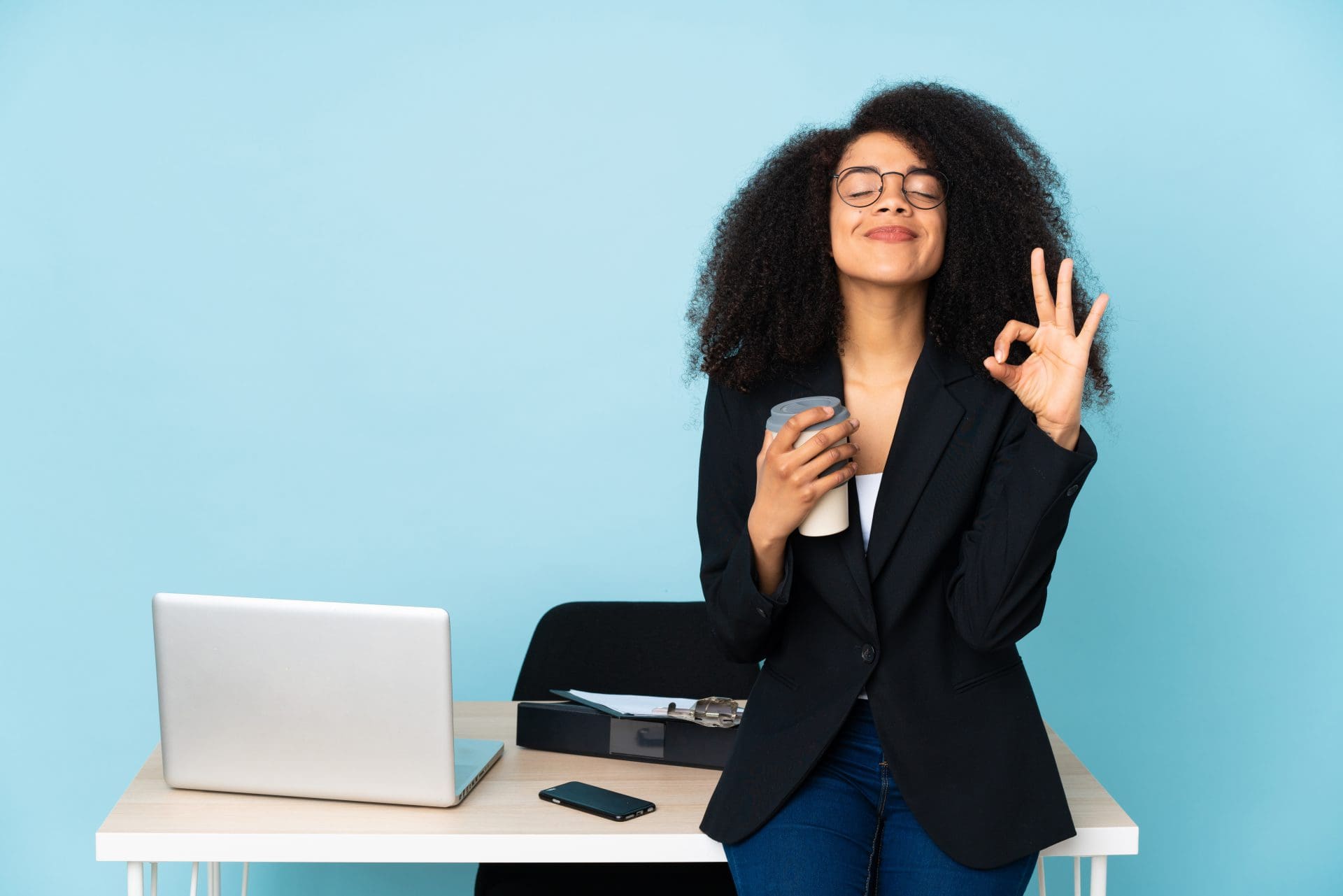 A happy and relaxed woman drinking coffee while leaning against their desk